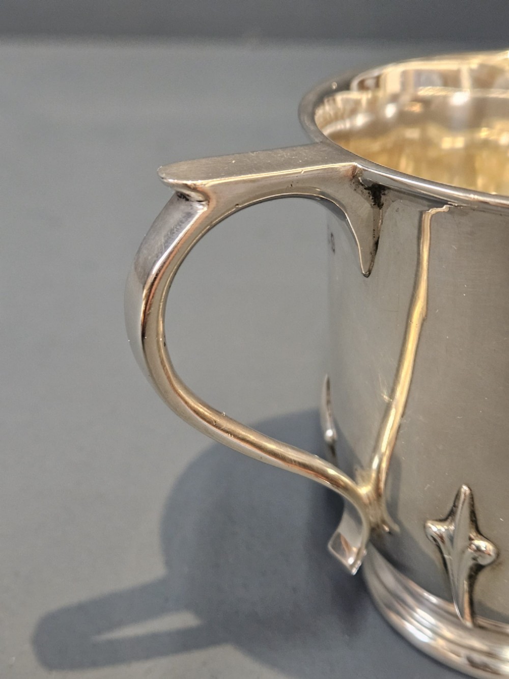 A hallmarked sterling silver mug with raised strapwork details around the lower body, a gilded interior, and a single loop handle. View VII