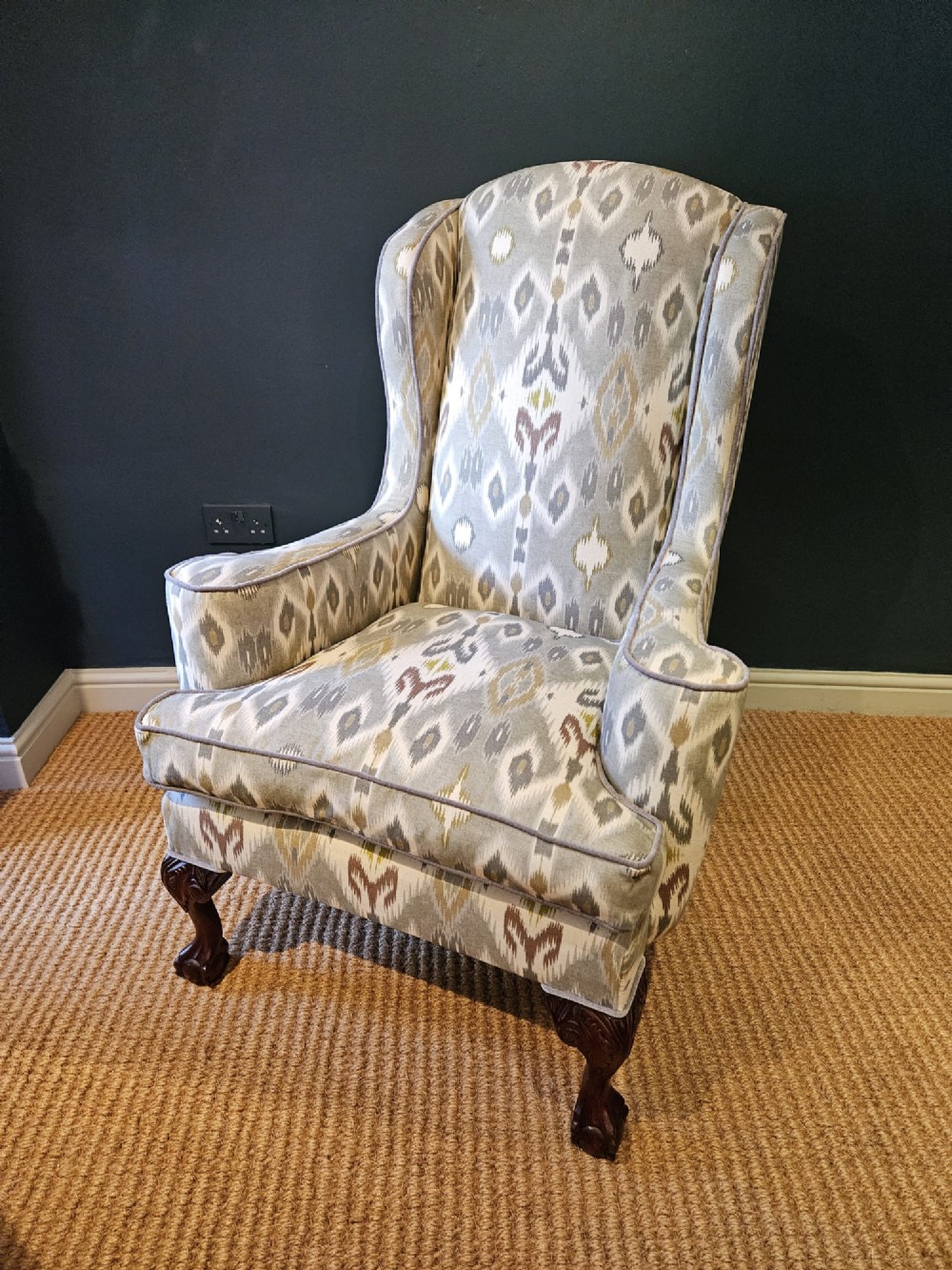An Edwardian wingback armchair upholstered in a patterned ikat fabric featuring grey and beige tones, supported by carved dark mahogany cabriole front legs.