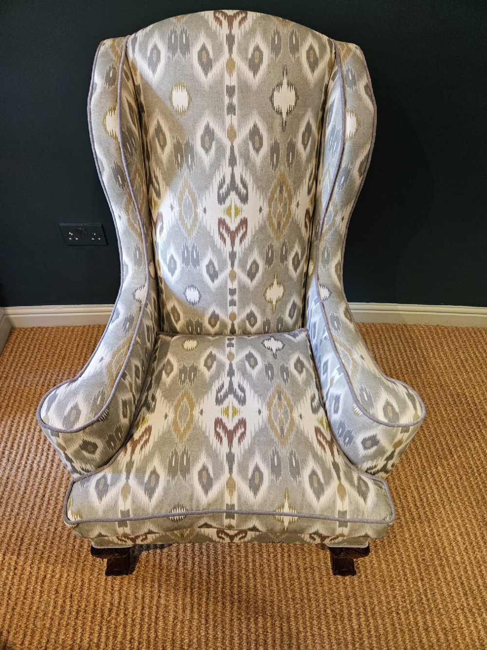 An Edwardian wingback armchair upholstered in a patterned ikat fabric featuring grey and beige tones, supported by carved dark mahogany cabriole front legs. View III