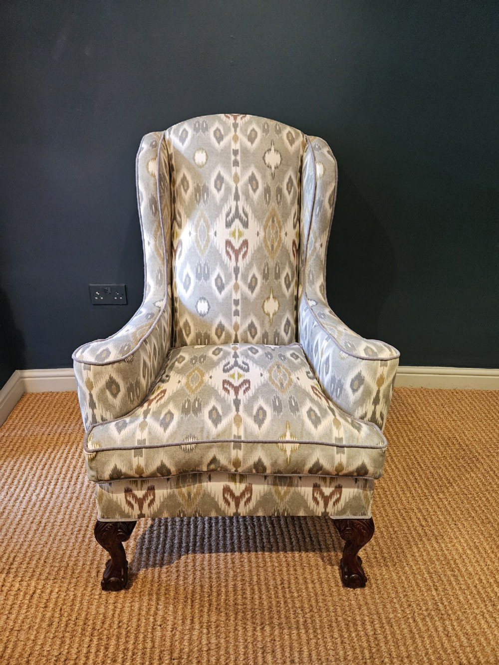 An Edwardian wingback armchair upholstered in a patterned ikat fabric featuring grey and beige tones, supported by carved dark mahogany cabriole front legs. View IV