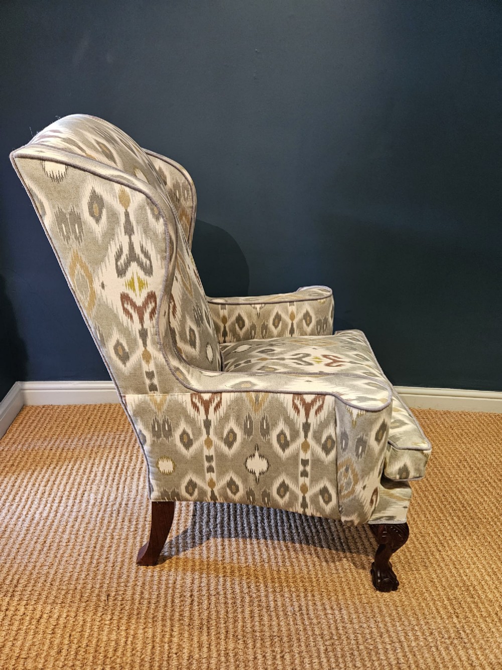 An Edwardian wingback armchair upholstered in a patterned ikat fabric featuring grey and beige tones, supported by carved dark mahogany cabriole front legs. View V