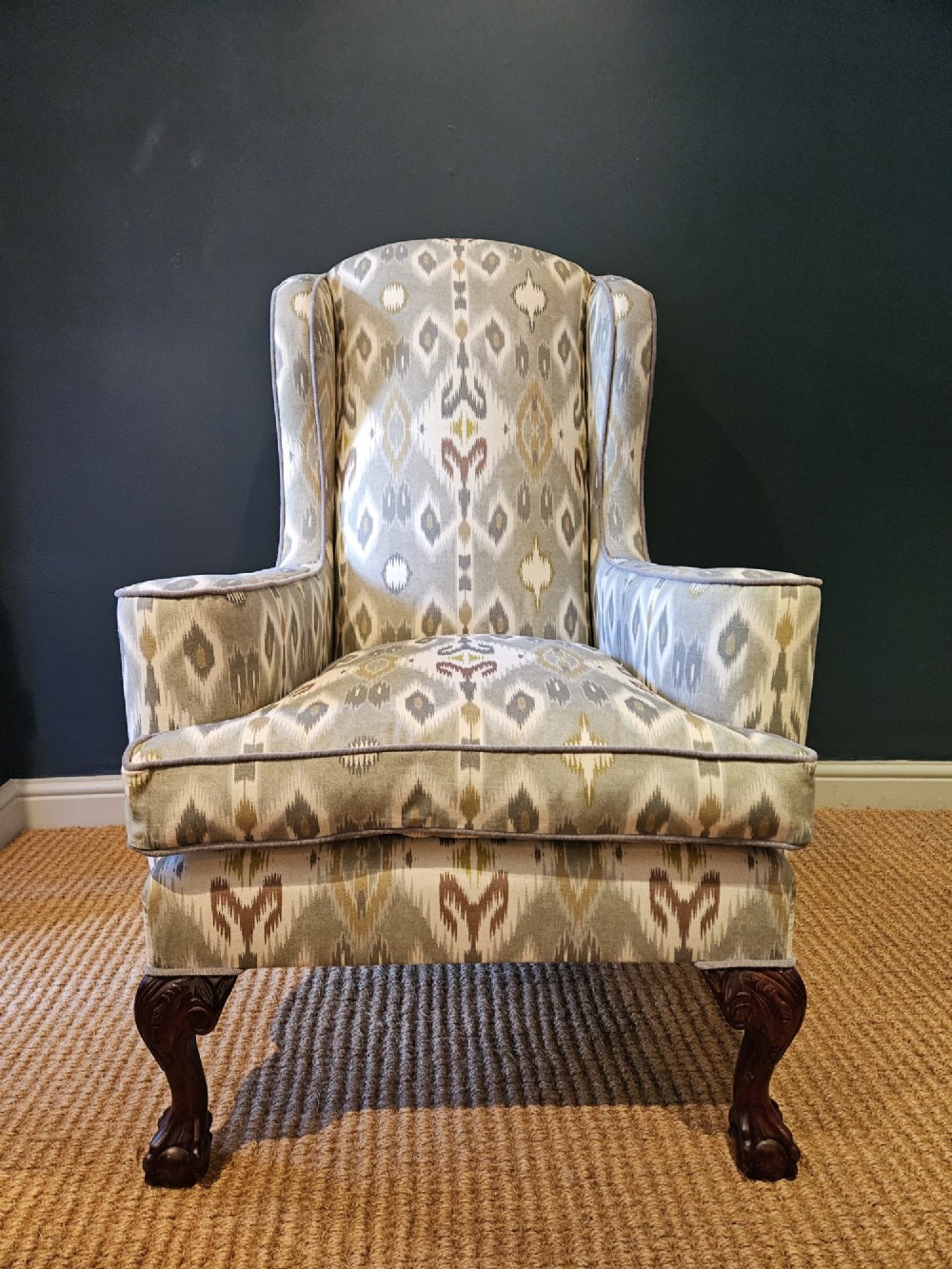 An Edwardian wingback armchair upholstered in a patterned ikat fabric featuring grey and beige tones, supported by carved dark mahogany cabriole front legs. View VI