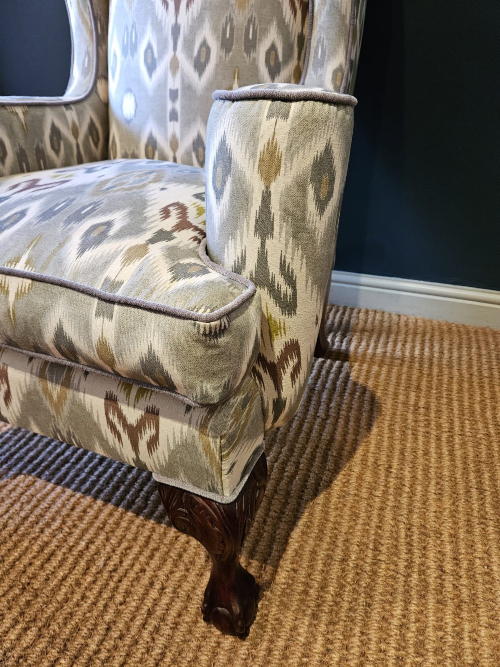 An Edwardian wingback armchair upholstered in a patterned ikat fabric featuring grey and beige tones, supported by carved dark mahogany cabriole front legs. View VII
