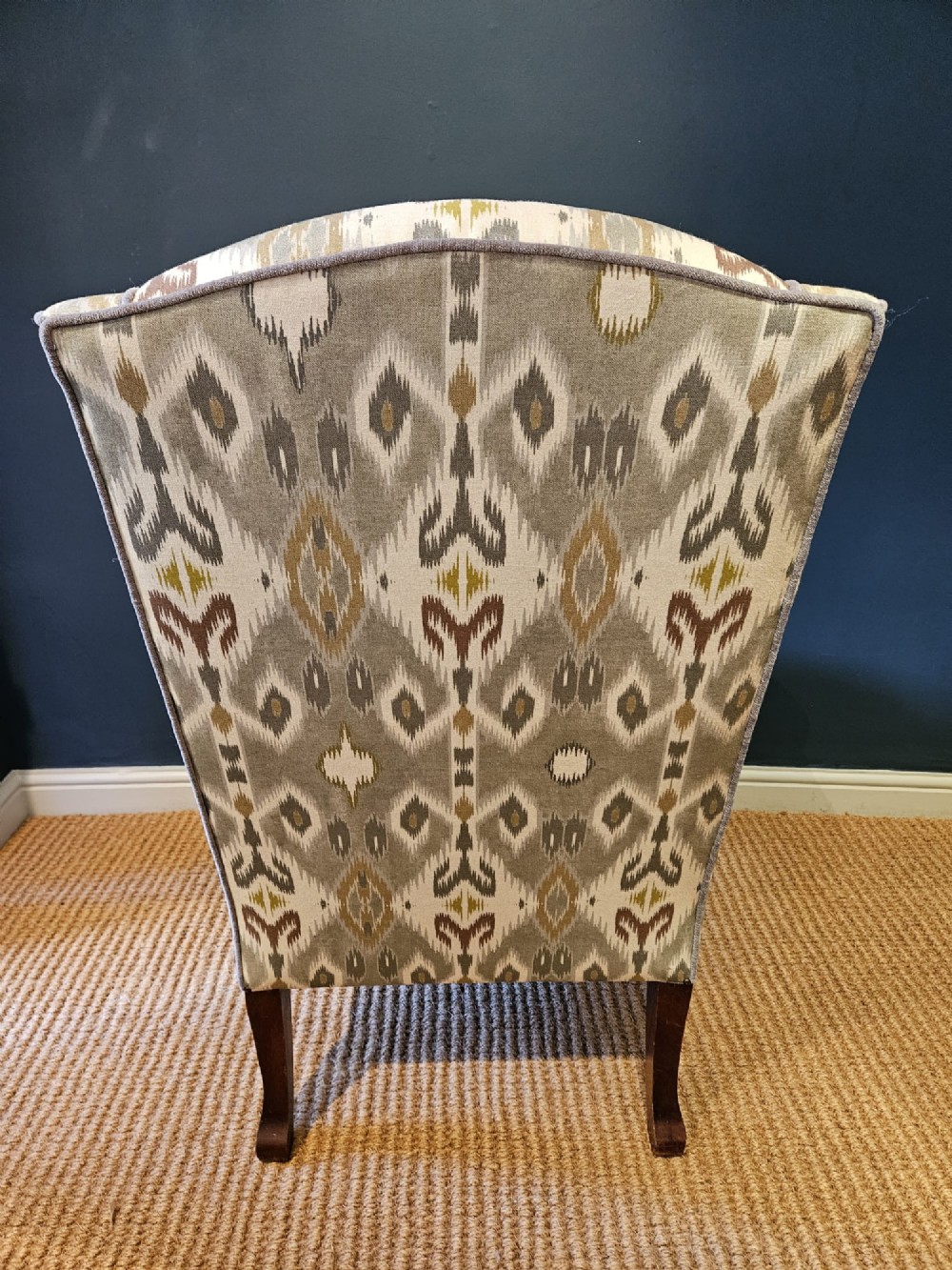 An Edwardian wingback armchair upholstered in a patterned ikat fabric featuring grey and beige tones, supported by carved dark mahogany cabriole front legs. View VIII