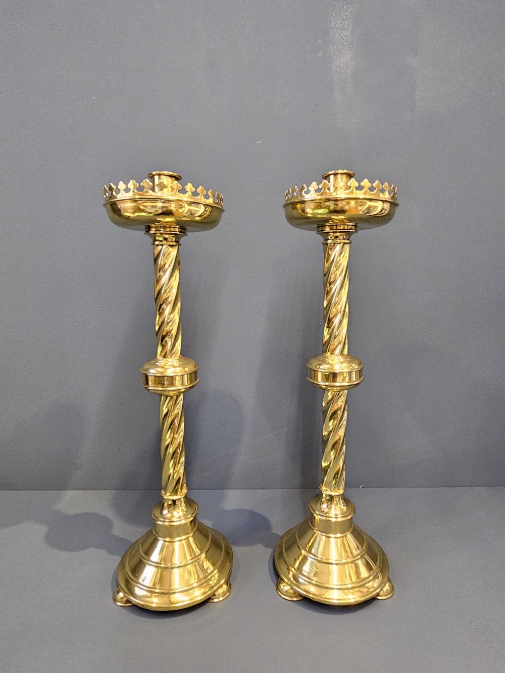A pair of tall, polished brass Victorian church candlesticks with barley twist stems, crenellated crowns, and circular stepped bases.