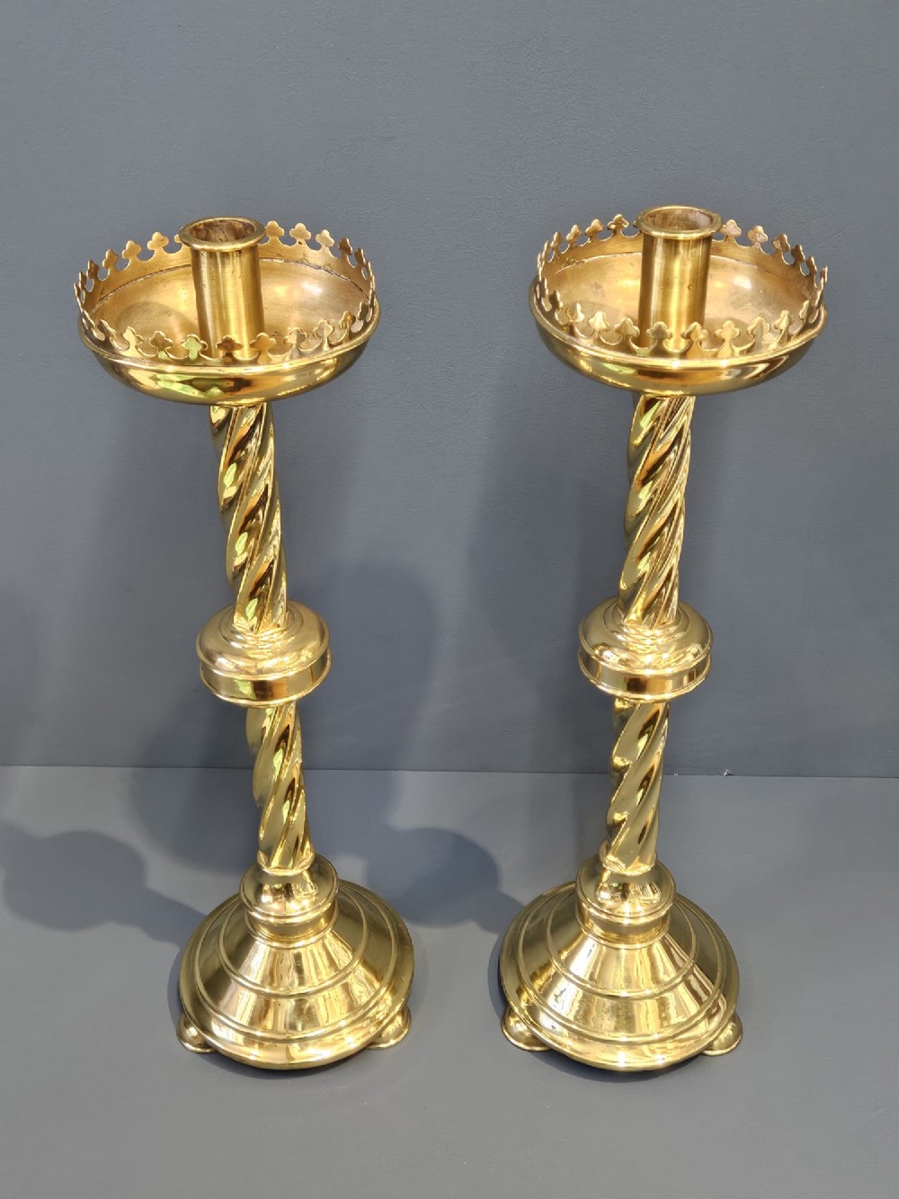 A pair of tall, polished brass Victorian church candlesticks with barley twist stems, crenellated crowns, and circular stepped bases. View IV
