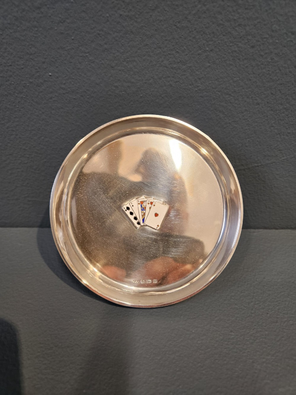 A circular sterling silver dish featuring a central polychrome enamel playing card fan design and stamped British hallmarks. View II