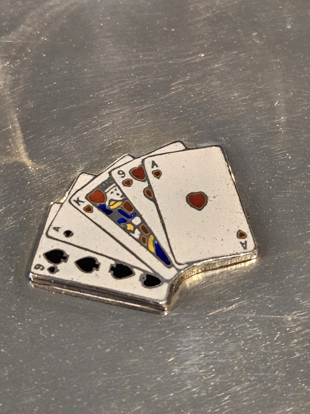 A circular sterling silver dish featuring a central polychrome enamel playing card fan design and stamped British hallmarks. View III