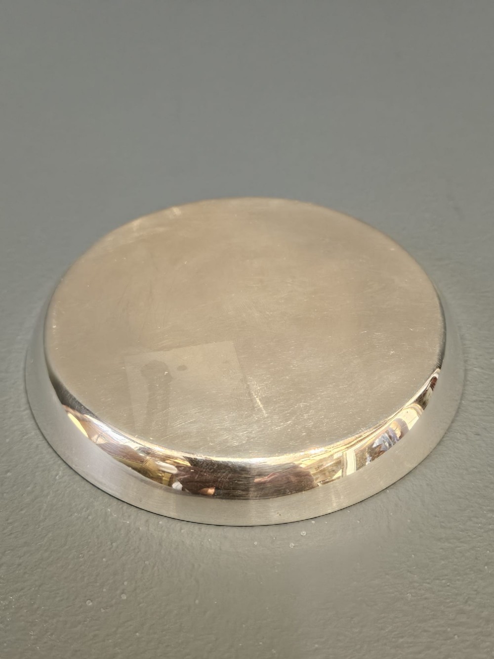 A circular sterling silver dish featuring a central polychrome enamel playing card fan design and stamped British hallmarks. View V