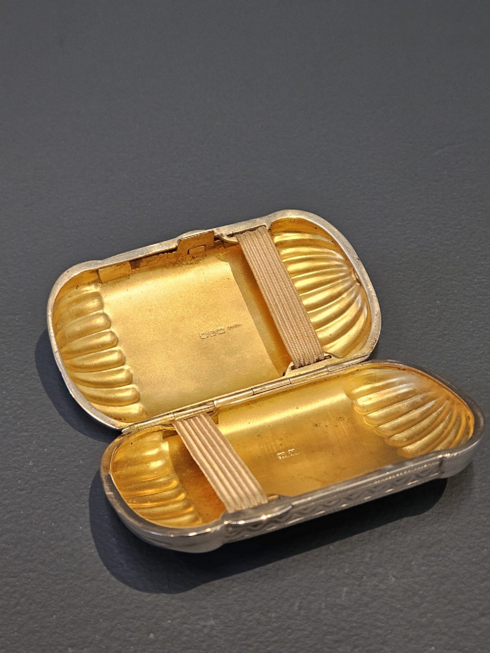 A small rectangular Victorian sterling silver cheroot case featuring hand-engraved foliate decoration and ribbed fluted ends on a grey surface. View III