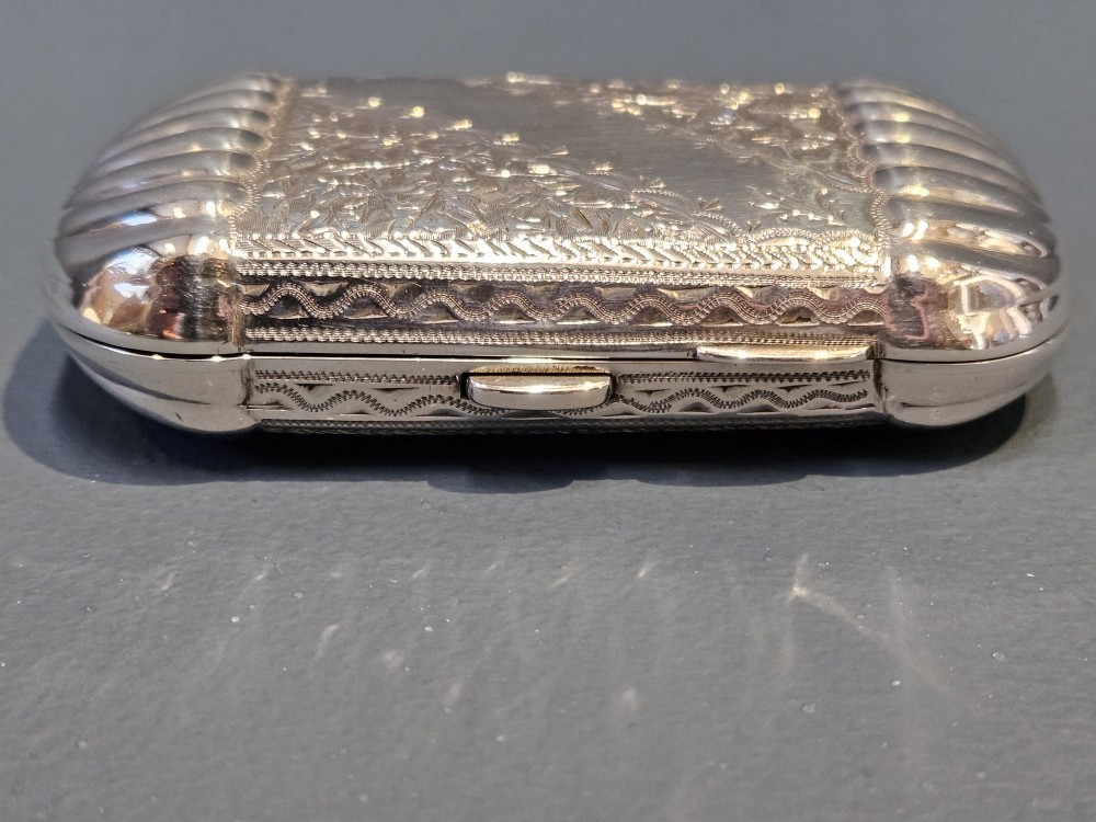A small rectangular Victorian sterling silver cheroot case featuring hand-engraved foliate decoration and ribbed fluted ends on a grey surface. View VI
