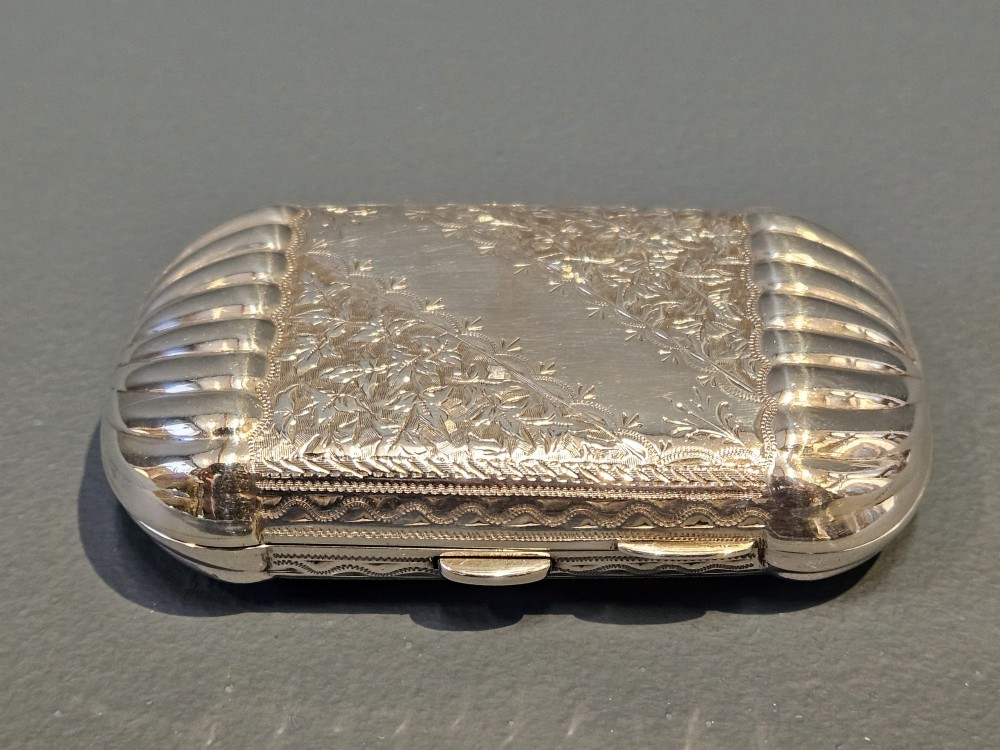 A small rectangular Victorian sterling silver cheroot case featuring hand-engraved foliate decoration and ribbed fluted ends on a grey surface. View VIII