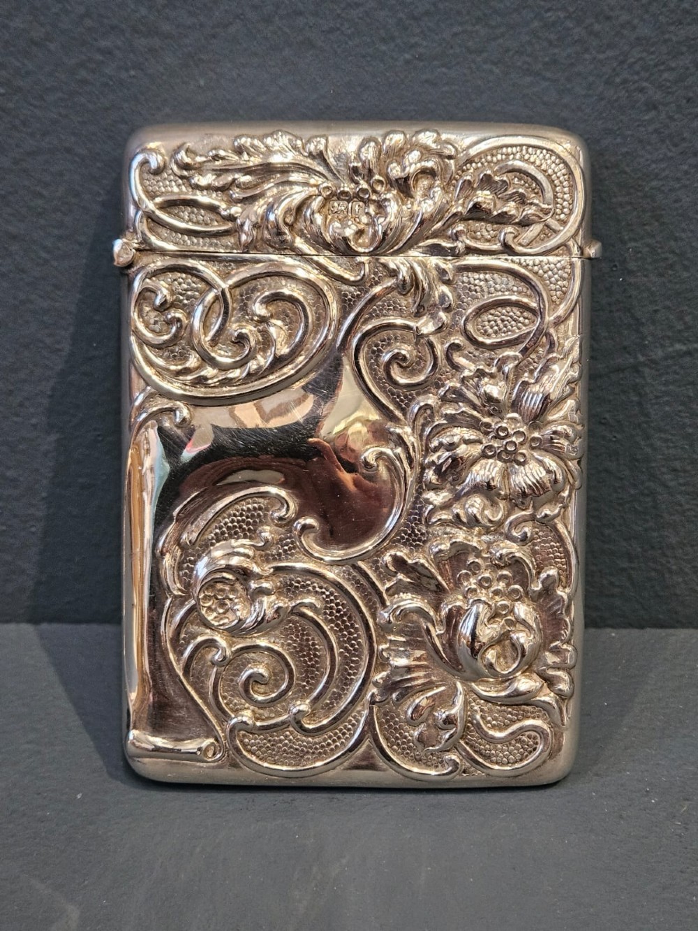 An Edwardian sterling silver hinged card case featuring intricate Art Nouveau repousse scrollwork and floral relief design.