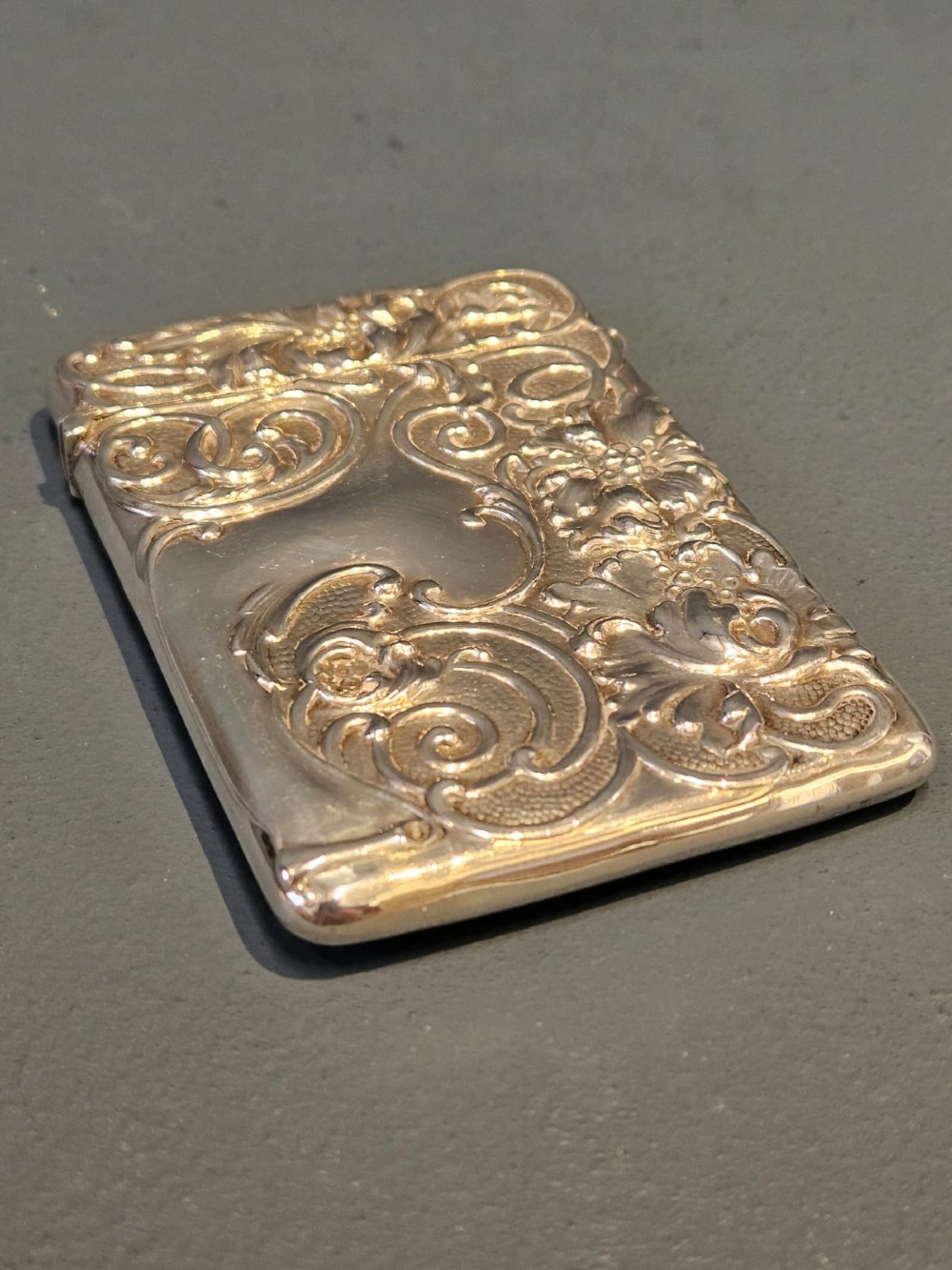 An Edwardian sterling silver hinged card case featuring intricate Art Nouveau repousse scrollwork and floral relief design. View V