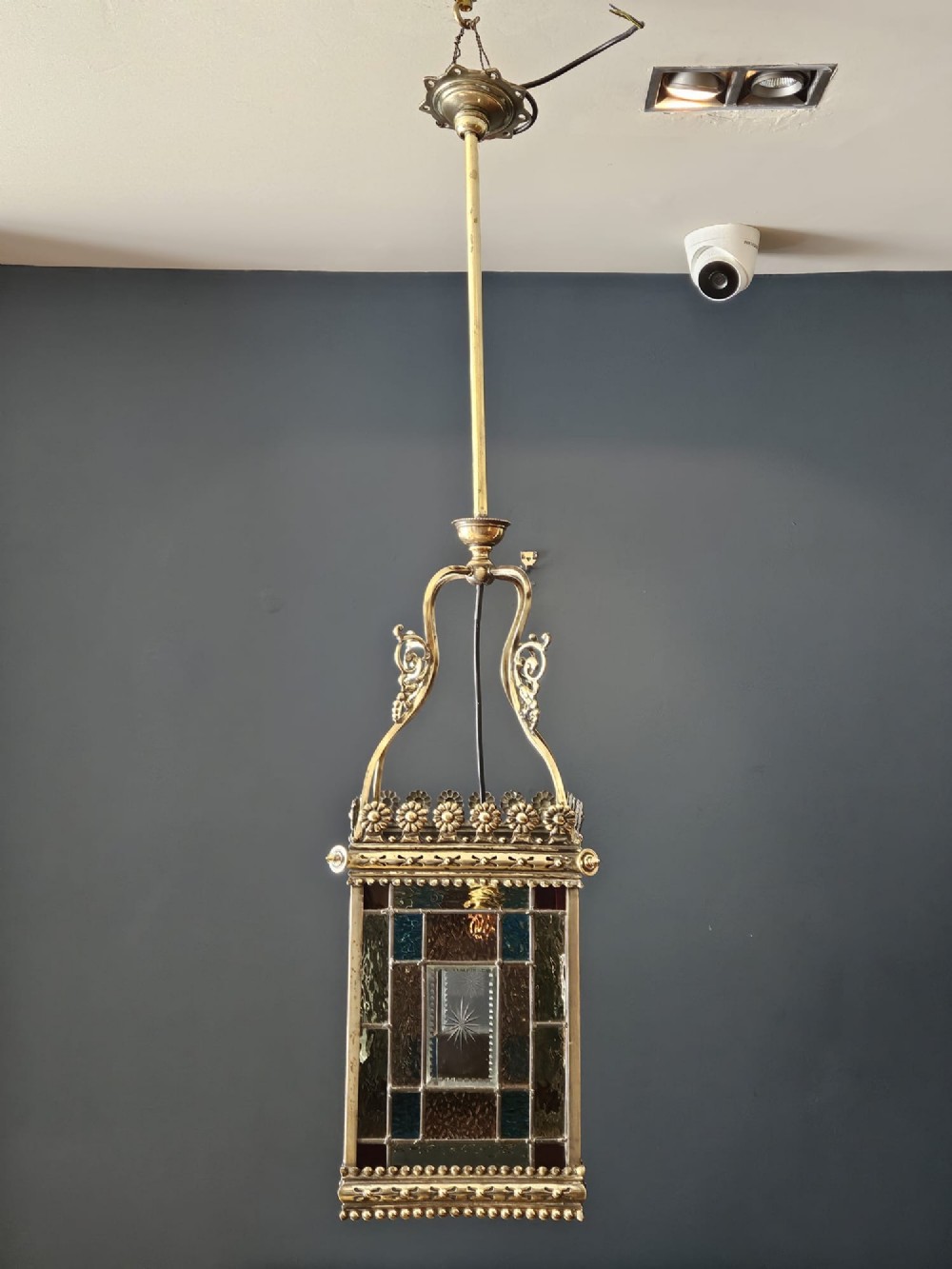 A Victorian brass hanging lantern featuring leaded stained-glass panels with starburst detailing and an ornate floral rim.