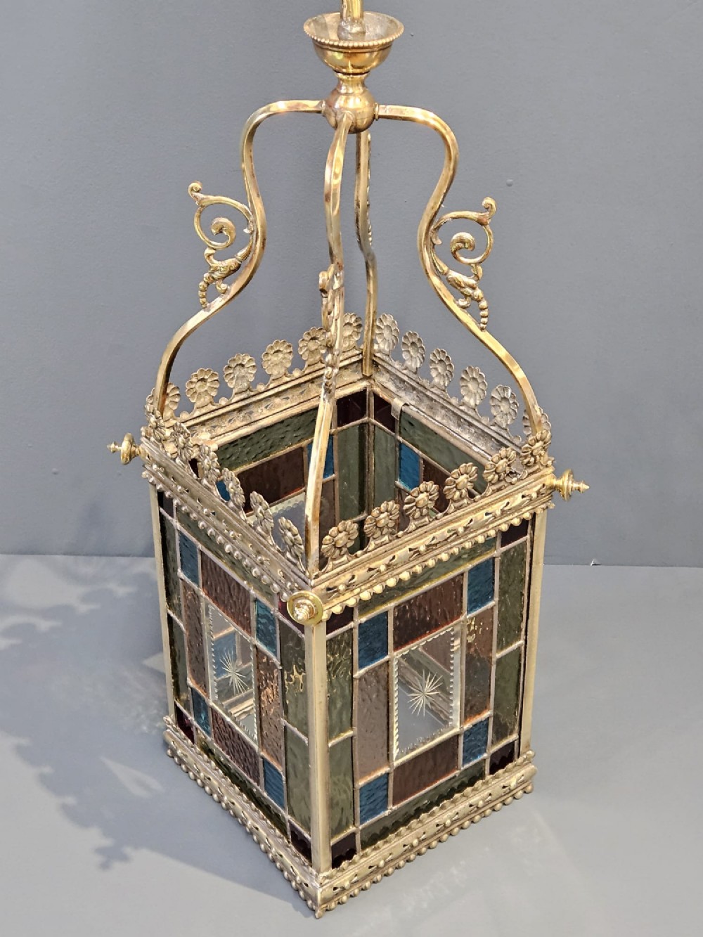 A Victorian brass hanging lantern featuring leaded stained-glass panels with starburst detailing and an ornate floral rim. View II