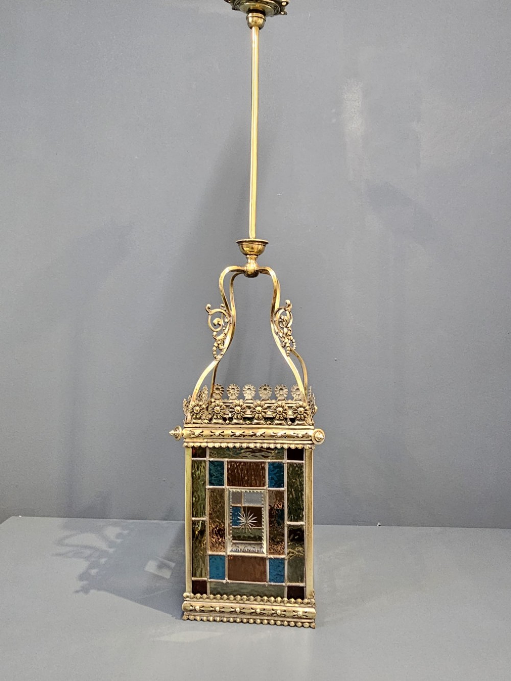 A Victorian brass hanging lantern featuring leaded stained-glass panels with starburst detailing and an ornate floral rim. View IV