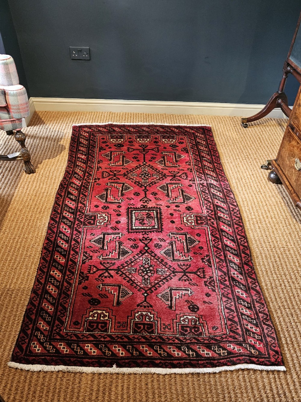 A hand-knotted deep red and dark brown Baluch tribal wool rug featuring geometric diamond medallions and short white fringe edges.