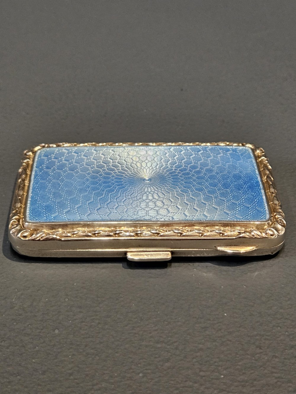 A rectangular silver case featuring a sky-blue engine-turned guilloche enamel panel and an ornate chased border.
