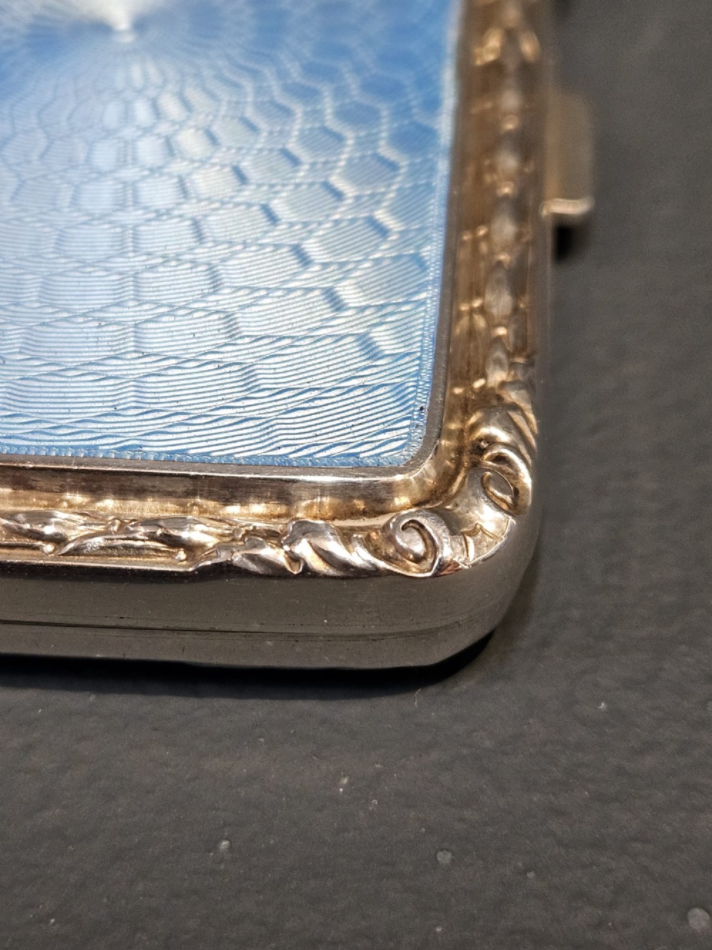 A rectangular silver case featuring a sky-blue engine-turned guilloche enamel panel and an ornate chased border. View V