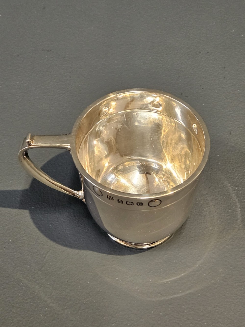 A polished sterling silver George V mug featuring riveted border detailing and a shaped handle. View VI