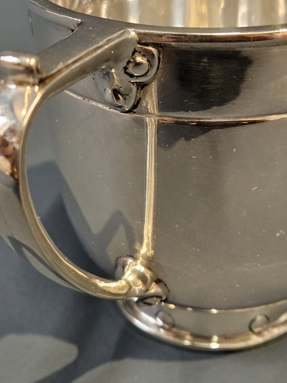 A polished sterling silver George V mug featuring riveted border detailing and a shaped handle. View VII
