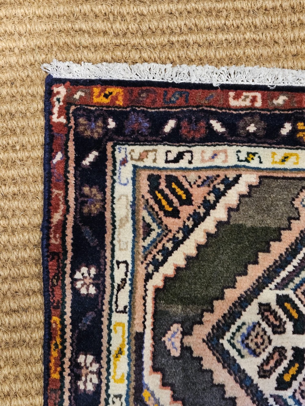 A long hand-woven wool runner rug featuring repeating diamond geometric medallions on an olive green background with decorative navy borders. View IV