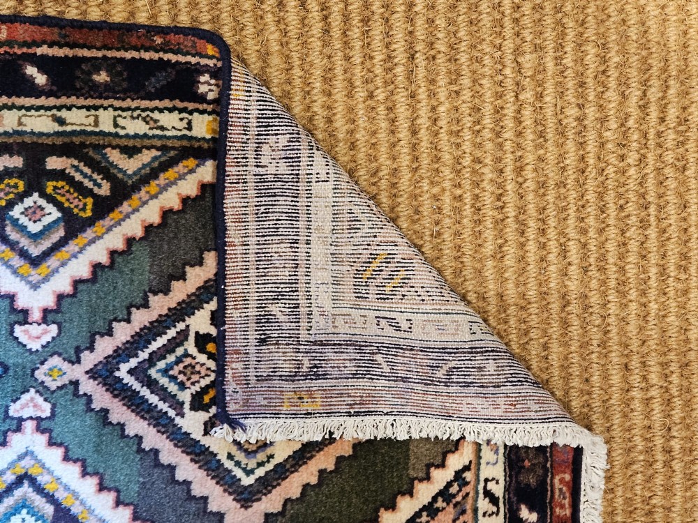A long hand-woven wool runner rug featuring repeating diamond geometric medallions on an olive green background with decorative navy borders. View VI