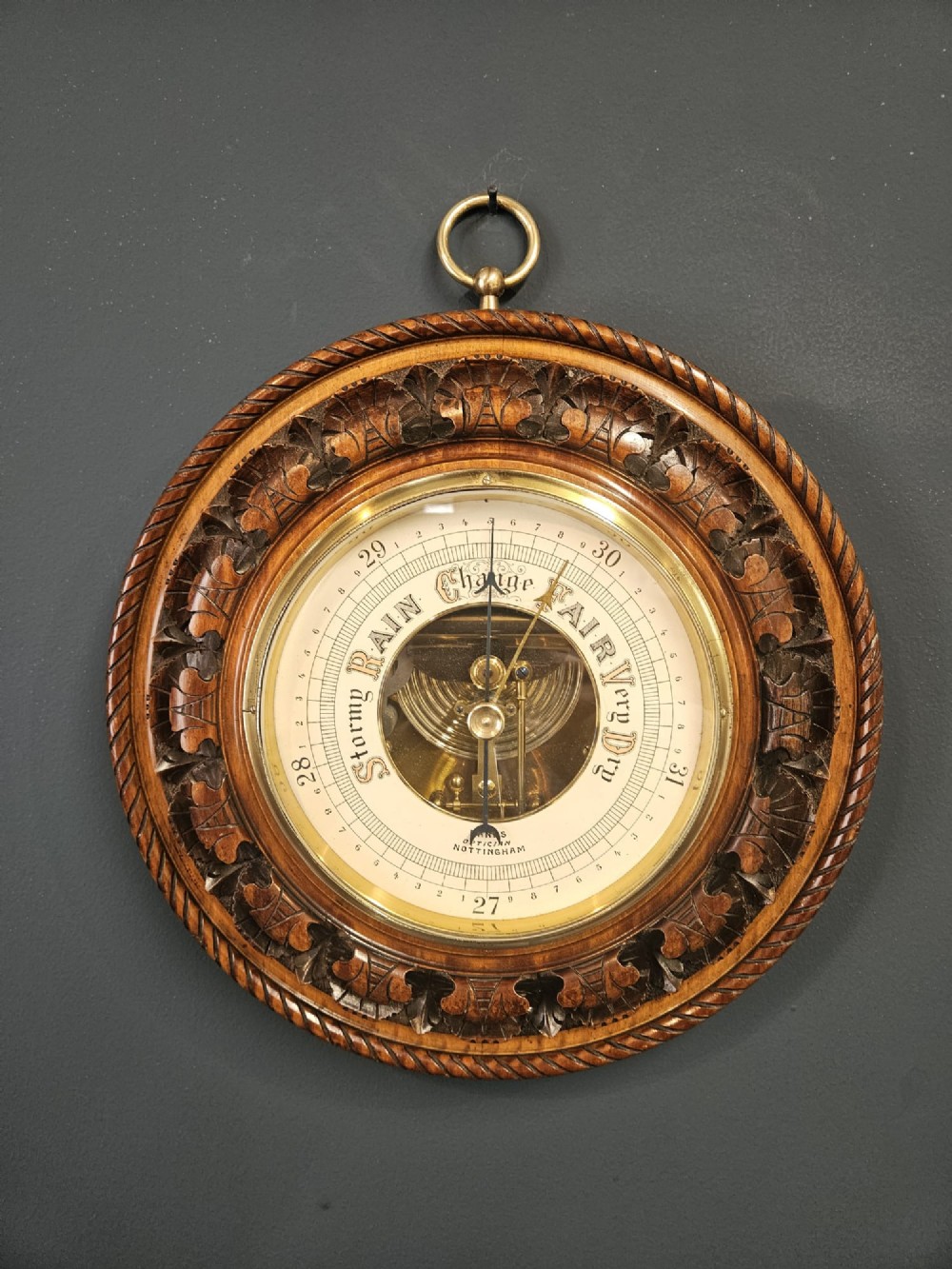 A circular Victorian carved walnut aneroid barometer featuring a rope twist border, leaf motifs, and an open centre dial exposing internal brass mechanisms.