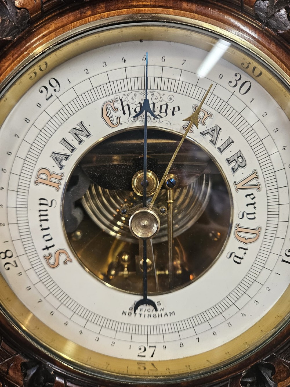 A circular Victorian carved walnut aneroid barometer featuring a rope twist border, leaf motifs, and an open centre dial exposing internal brass mechanisms. View II