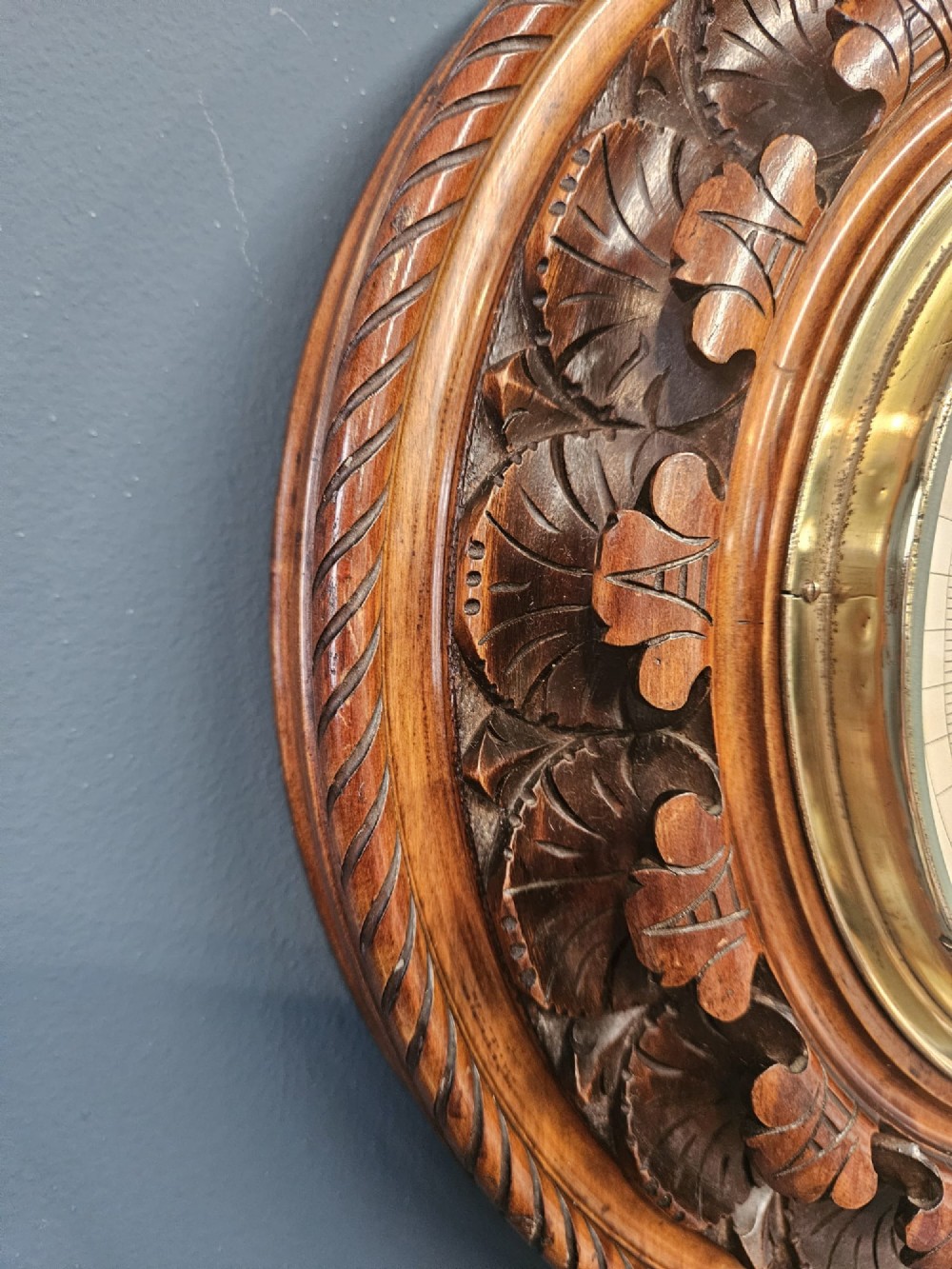 A circular Victorian carved walnut aneroid barometer featuring a rope twist border, leaf motifs, and an open centre dial exposing internal brass mechanisms. View III