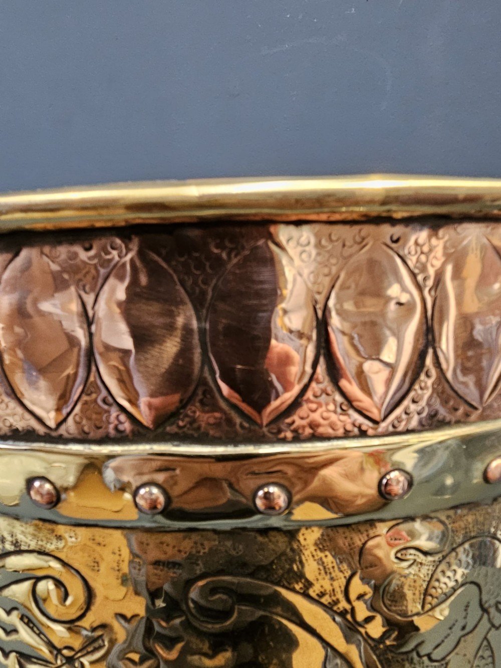 A circular Victorian brass log bin featuring embossed pictorial scenes, a copper rim, cast lion mask side handles, and paw feet. View V