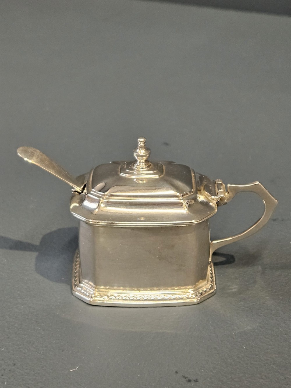 A cased five-piece silver cruet set featuring two pepper casters, two open salt cellars with blue glass liners, a mustard pot, and three spoons inside a silk-lined box. View VII