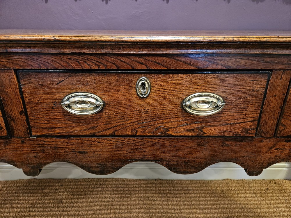 An 18th-century George II elm low dresser featuring three drawers with brass bail handles and shaped cabriole legs. View II