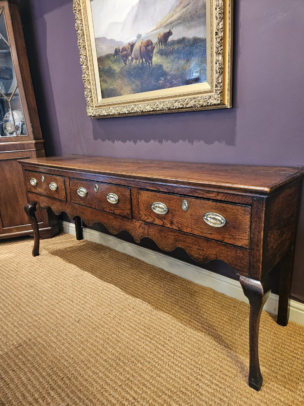 An 18th-century George II elm low dresser featuring three drawers with brass bail handles and shaped cabriole legs. View IX