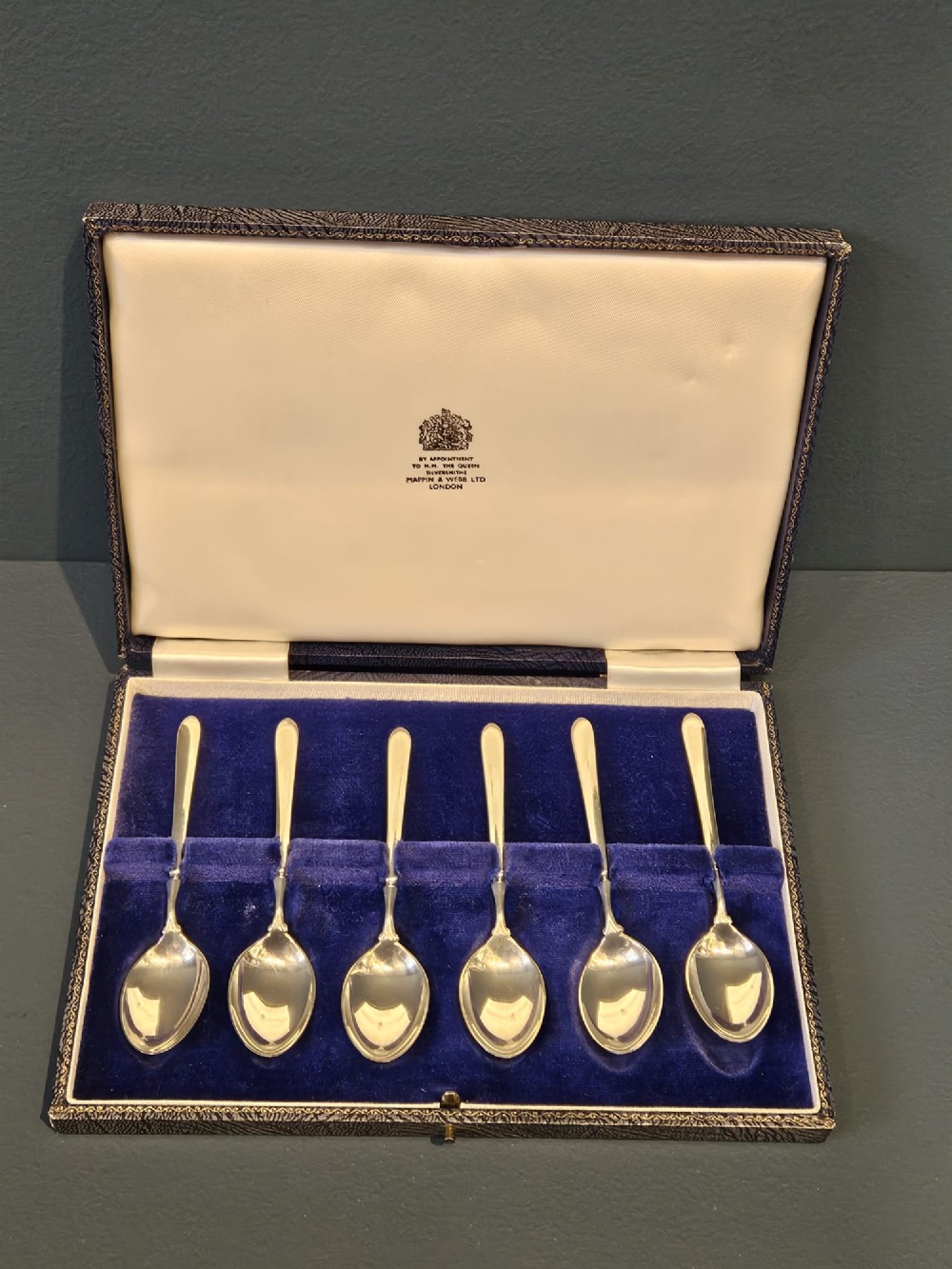 A set of six silver coffee spoons displayed inside a dark fitted presentation case lined with blue velvet and white silk. View VI