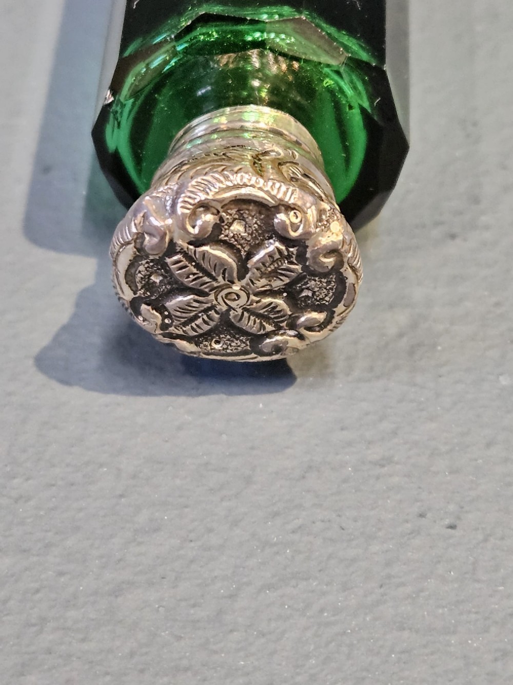 A Victorian double-ended emerald green facet-cut glass scent bottle with detailed embossed silver caps on both ends. View II