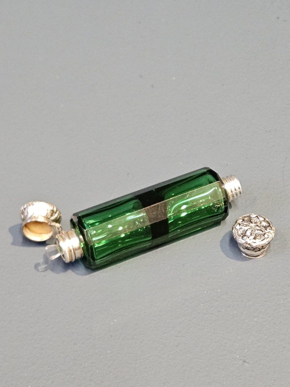 A Victorian double-ended emerald green facet-cut glass scent bottle with detailed embossed silver caps on both ends. View III