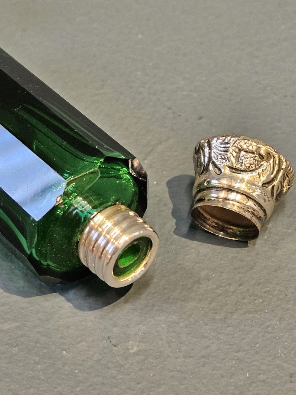 A Victorian double-ended emerald green facet-cut glass scent bottle with detailed embossed silver caps on both ends. View V