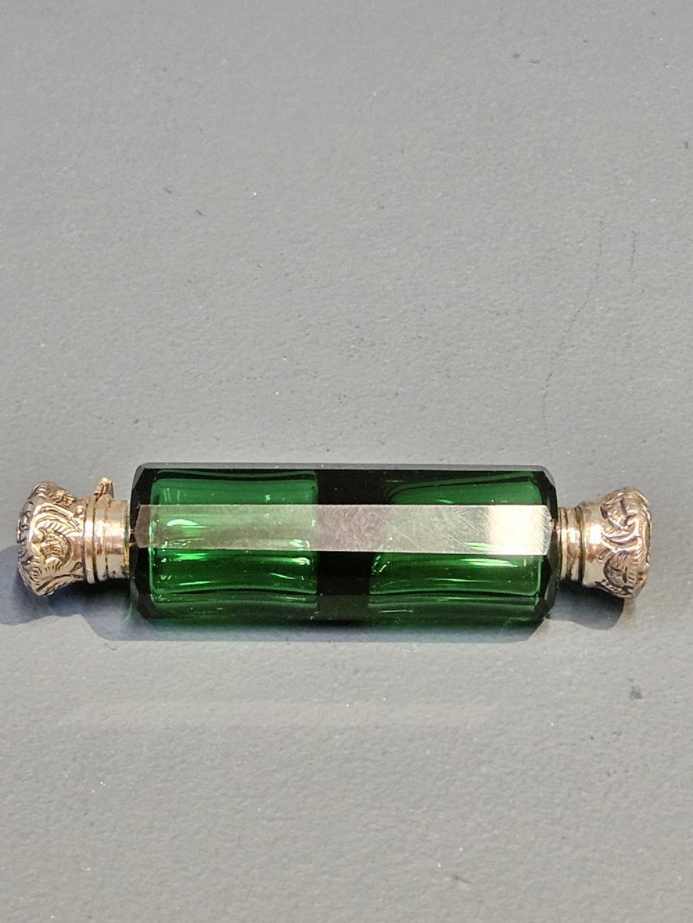 A Victorian double-ended emerald green facet-cut glass scent bottle with detailed embossed silver caps on both ends. View VIII