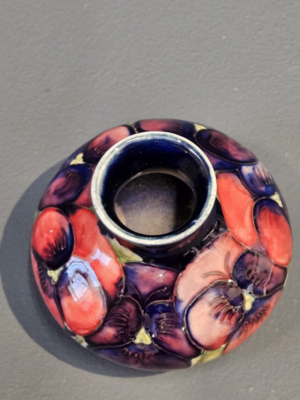 A small squat earthenware vase featuring a dark cobalt blue glaze decorated with hand-painted purple and pink pansy motifs. View IV