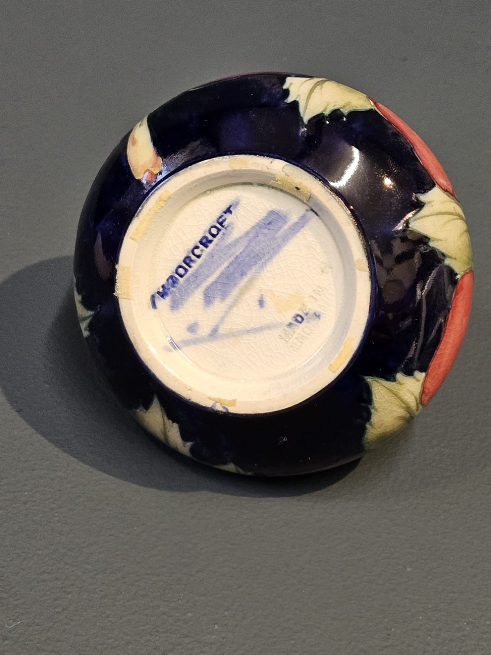 A small squat earthenware vase featuring a dark cobalt blue glaze decorated with hand-painted purple and pink pansy motifs. View VI