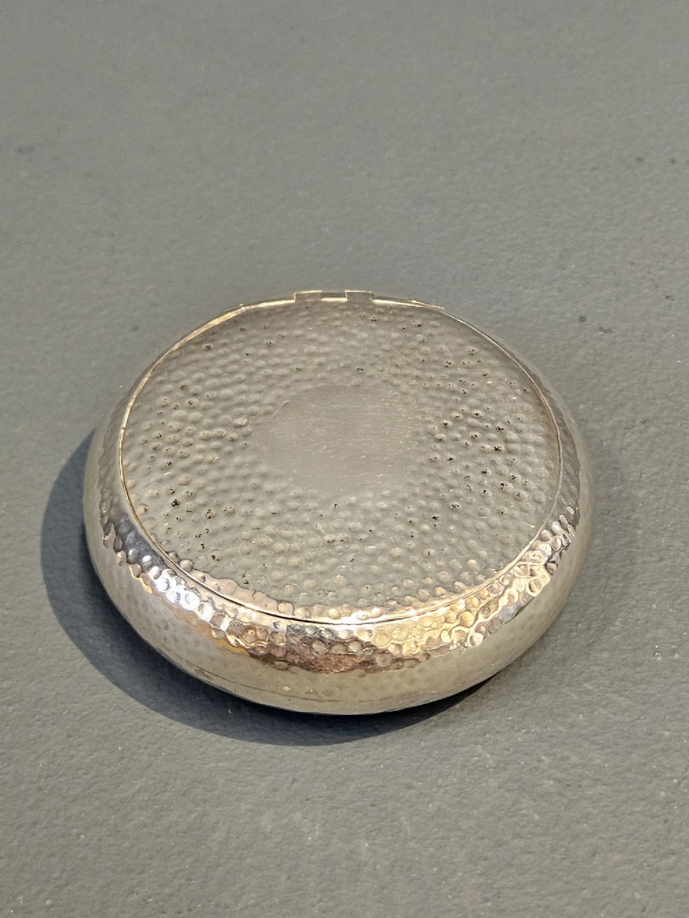 A round, pebble-shaped sterling silver box with a hand-hammered planished texture and smooth central circular cartouche. View II