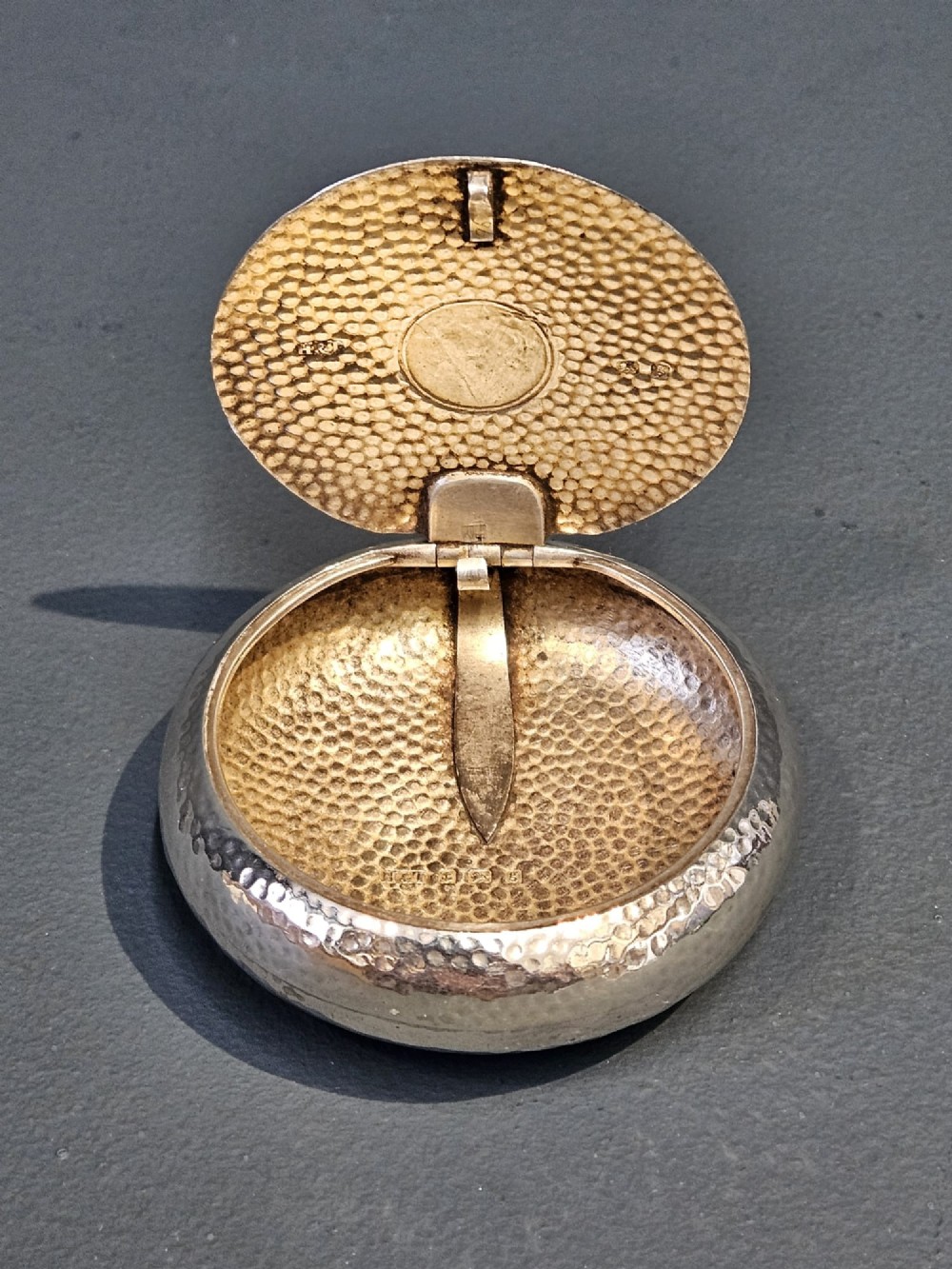 A round, pebble-shaped sterling silver box with a hand-hammered planished texture and smooth central circular cartouche. View III