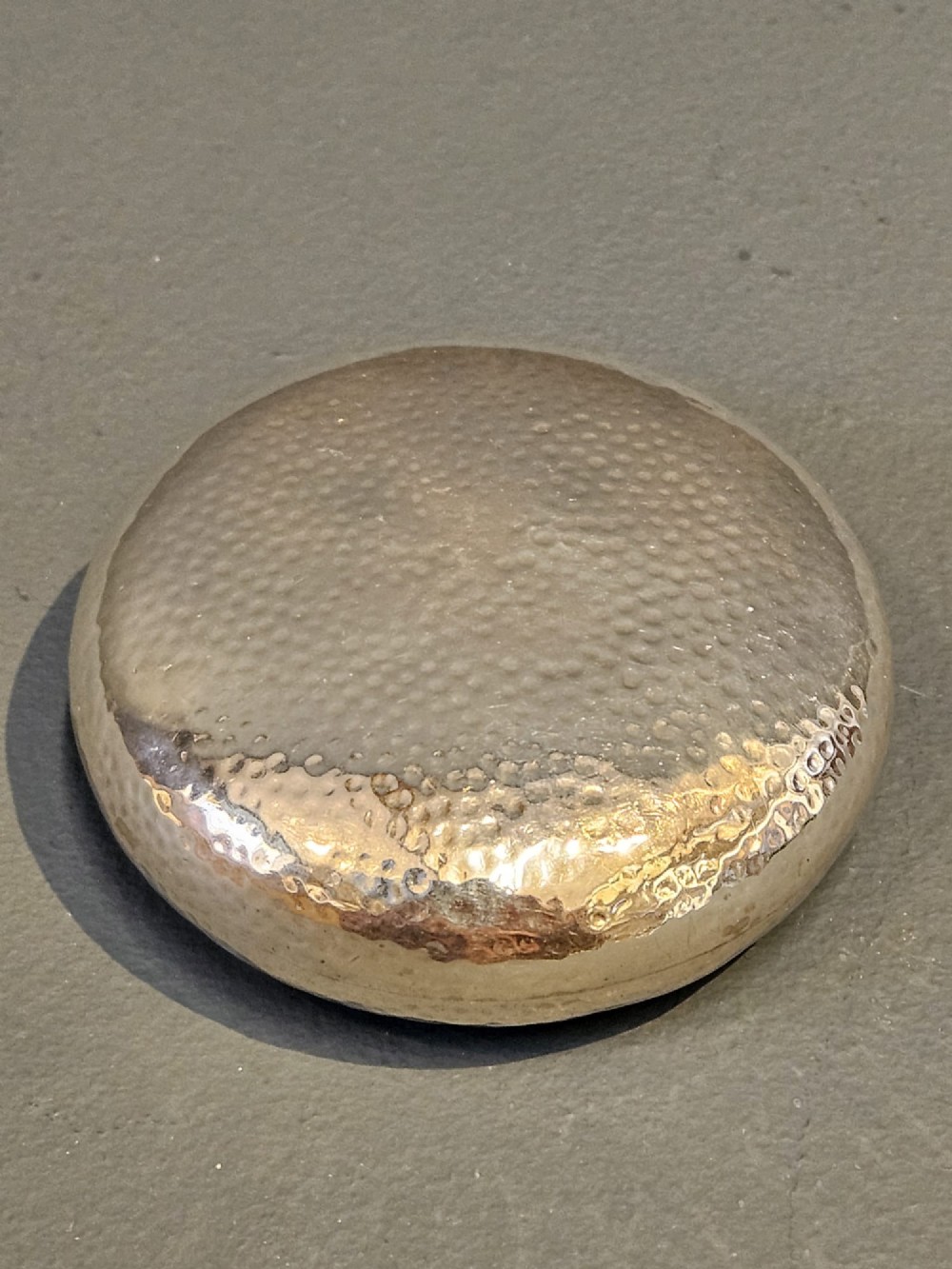 A round, pebble-shaped sterling silver box with a hand-hammered planished texture and smooth central circular cartouche. View V
