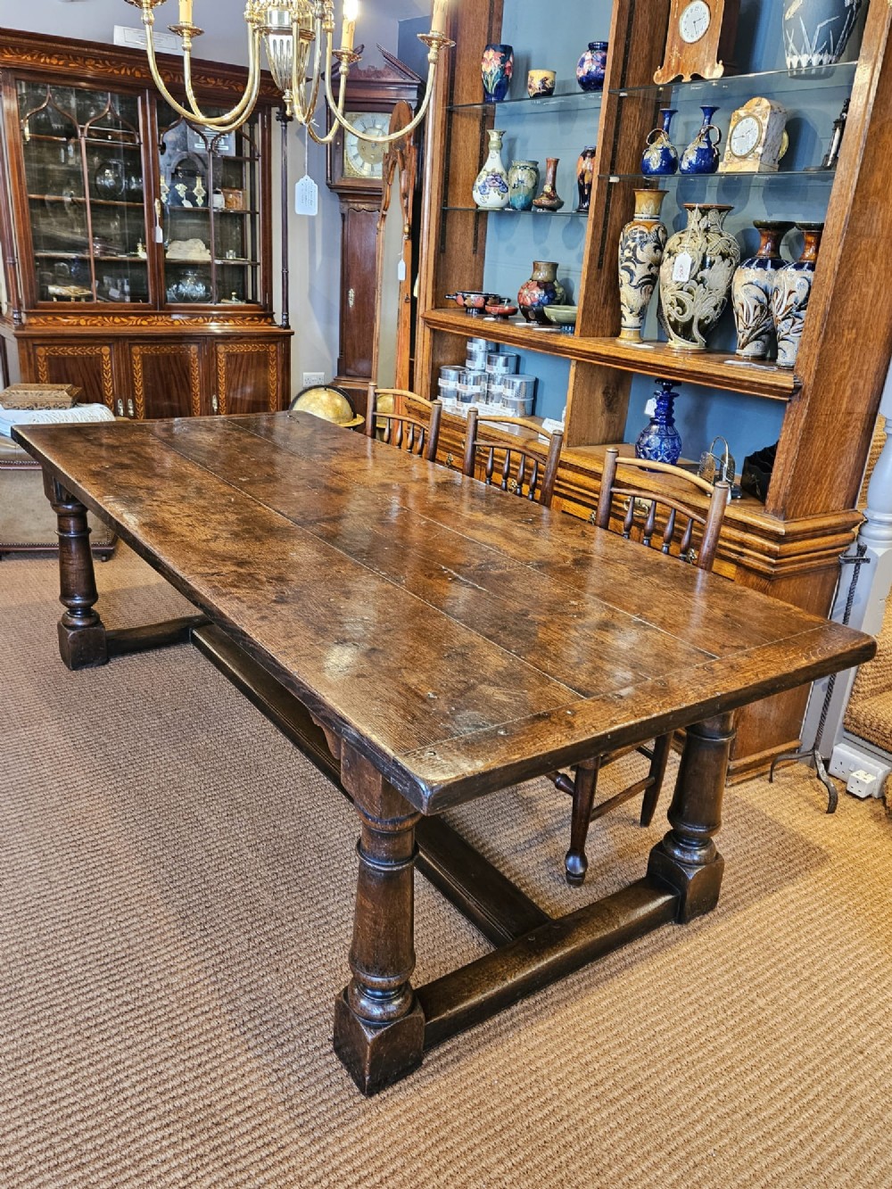 A large George III dark oak refectory dining table featuring a solid plank top, turned legs, and a low H-stretcher base. View II