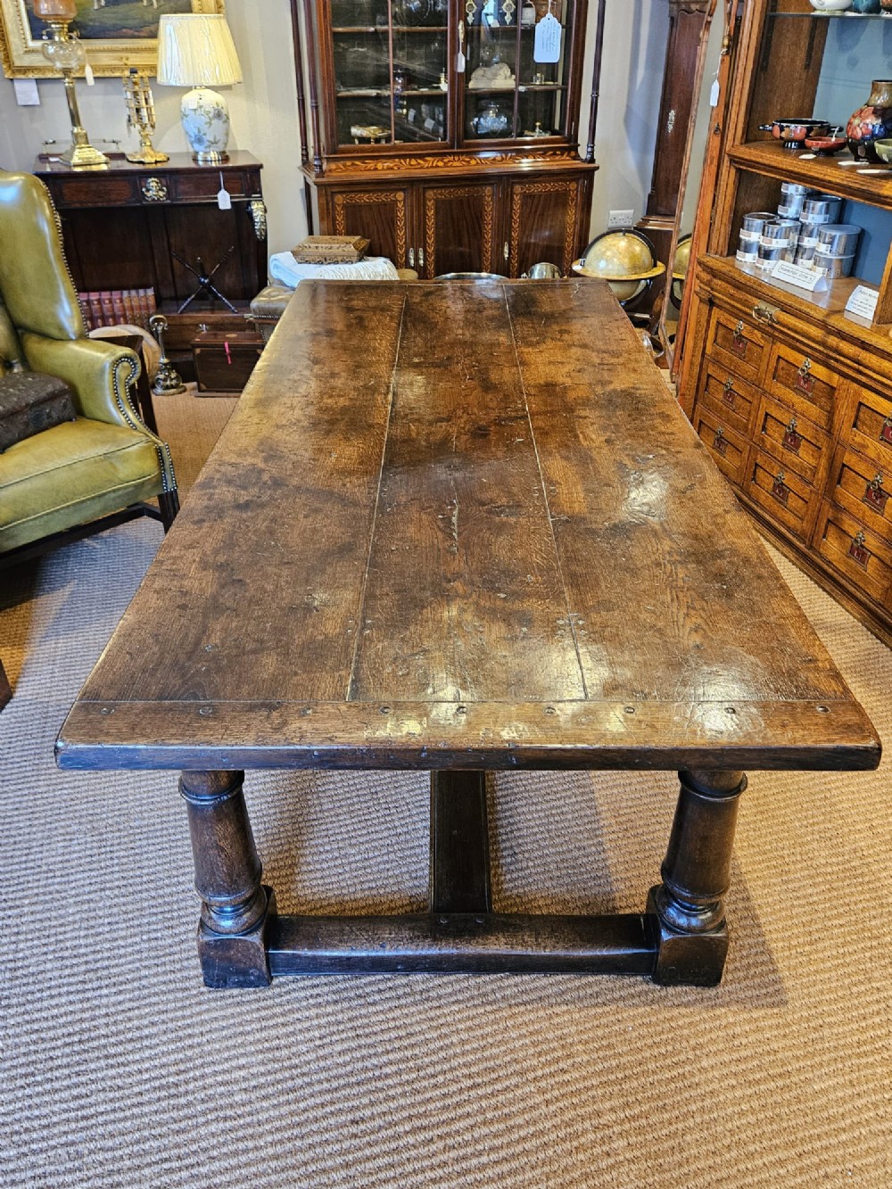 A large George III dark oak refectory dining table featuring a solid plank top, turned legs, and a low H-stretcher base. View III