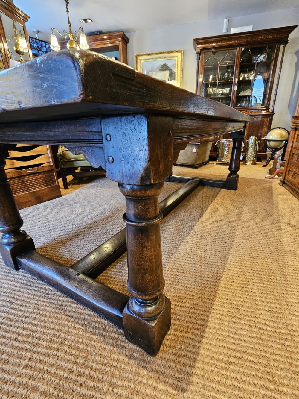 A large George III dark oak refectory dining table featuring a solid plank top, turned legs, and a low H-stretcher base. View V