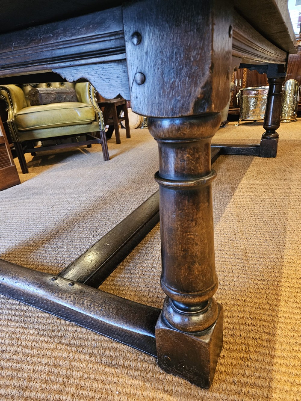 A large George III dark oak refectory dining table featuring a solid plank top, turned legs, and a low H-stretcher base. View VII