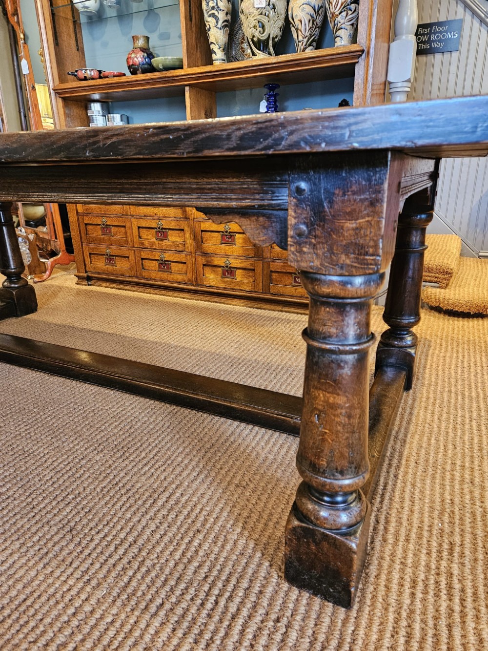 A large George III dark oak refectory dining table featuring a solid plank top, turned legs, and a low H-stretcher base. View IX